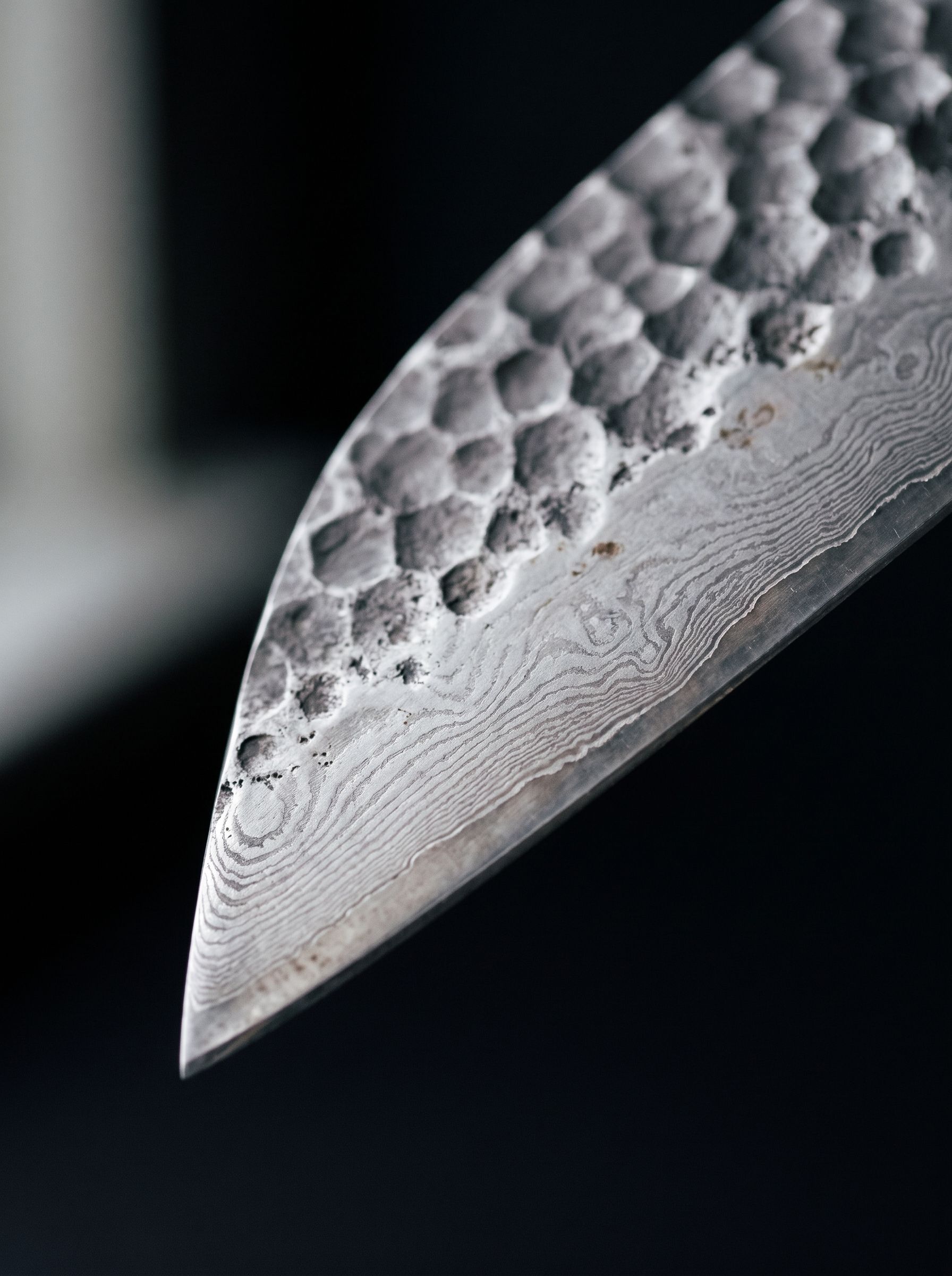 Macro close-up of the santoku blade’s hammered tsuchime dimples and layered steel grain.